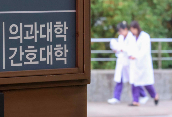 Two people in white medical gown are seen in front of a medical college building in Seoul in last month. [YONHAP]