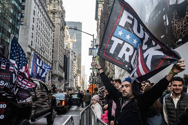 미국 뉴욕에서 지난 9일(현지시간) 도널드 트럼프 전 대통령의 당선을 축하하는 차량 옆에 트럼프 당선인을 비판하는 이가 ‘트럼프 엿먹어라’가 적힌 현수막을 펼치고 있다. AFP연합뉴스