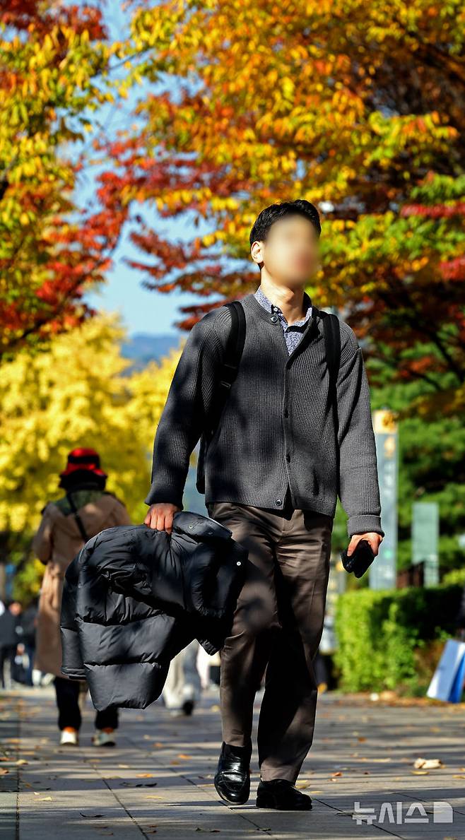 [서울=뉴시스] 김금보 기자 = 서울 낮 기온이 17까지 오르며 포근한 늦가을 날씨를 보인 8일 서울 거리에서 시민이 외투를 벗어들고 걸어가고 있다. 2024.11.08. kgb@newsis.com