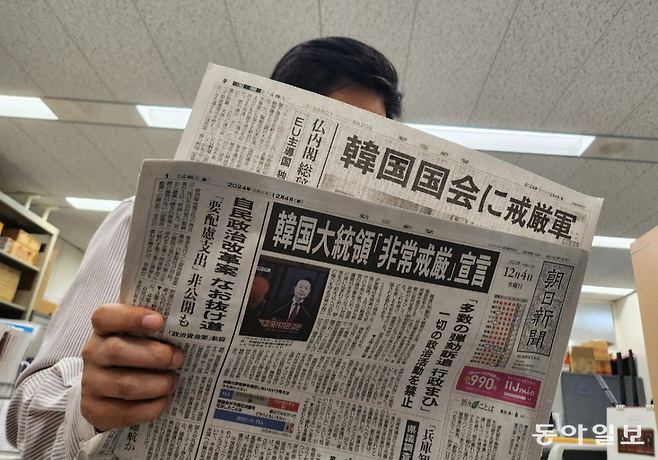4일 일본 도쿄의 한 시민이 윤석열 대통령의 비상계엄 선포 및 해제 관련 소식을 1면 머리기사로 다룬 아사히신문을 읽고 있다. 도쿄=이상훈 특파원 sanghun@donga.com
