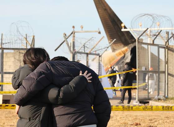 Bereaved families of those killed in the fatal crash at Muan International Airport, South Jeolla, sheds tears looking onto the remnants of the wrecked plane on Dec. 30. [YONHAP]