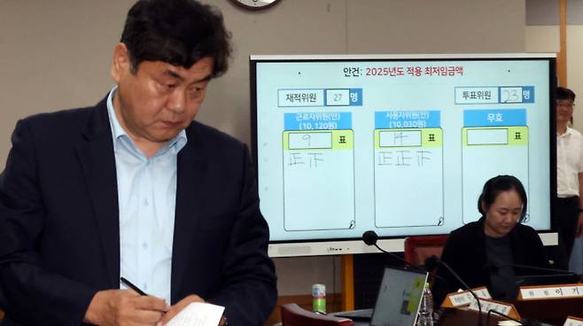 이인재 최저임금위원장이 지난 7월12일 새벽 세종시 정부세종청사에서 2025년도 적용 최저임금이 결정된 뒤 자리로 향하고 있다. 뒤쪽으로 내년도 최저임금은 10030원 결정된 표결결과가 보이고 있다. /사진=뉴시스