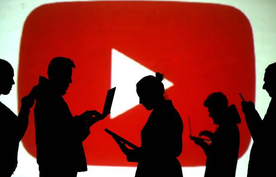 Silhouettes of laptop and mobile device users are seen next to a screen projection of the YouTube logo in this picture illustration taken on March 28, 2018. [REUTERS/YONHAP]