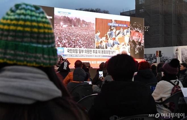 [광주=뉴시스]변재훈 기자 = 7일 오후 광주 동구 5·18민주광장에서 열린 정권 퇴진 4차 총궐기 대회에 참석한 시민들이 국회 본회의장 윤석열 대통령 탄핵소추안 의결 중계 장면을 지켜보고 있다. 2024.12.07. wisdom21@newsis.com /사진=