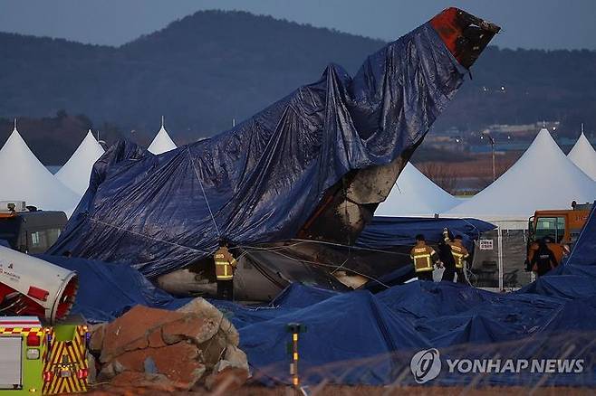 제주항공 무안공항 참사 7일째인 4일 오후 수색 작업이 끝난 사고 현장에서 소방대원들이 꼬리 날개에 방수포를 덮고 있다ⓒ연합뉴스