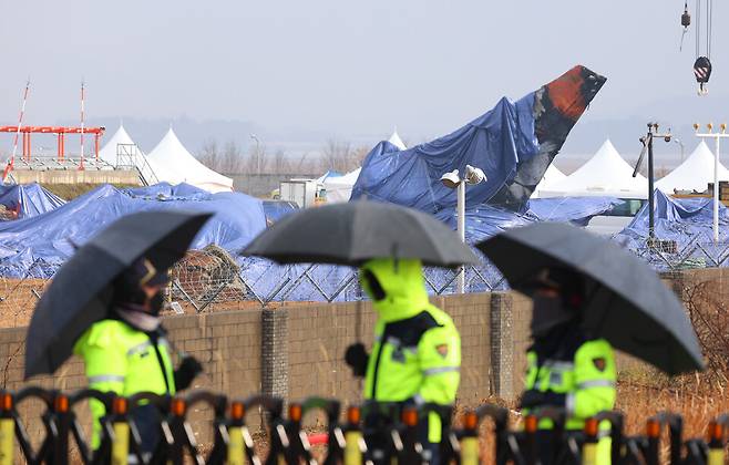 5일 오전 우산을 쓰고 근무하는 경찰관들 뒤로 전남 무안국제공항 사고현장 및 꼬리 날개에 방수포가 덮여 있다. ⓒ연합뉴스