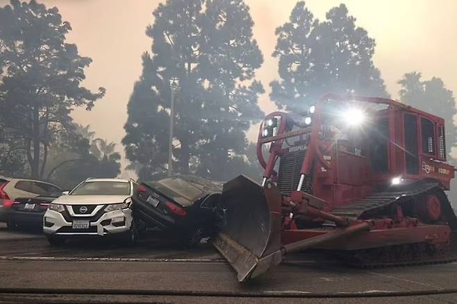 7일(현지시간)  퍼시픽 팰리세이즈 산불 현장에서 구급대원이 불도저를 동원해 거리에서 버려진 차량을 치우고 있다 [zuma press wire]