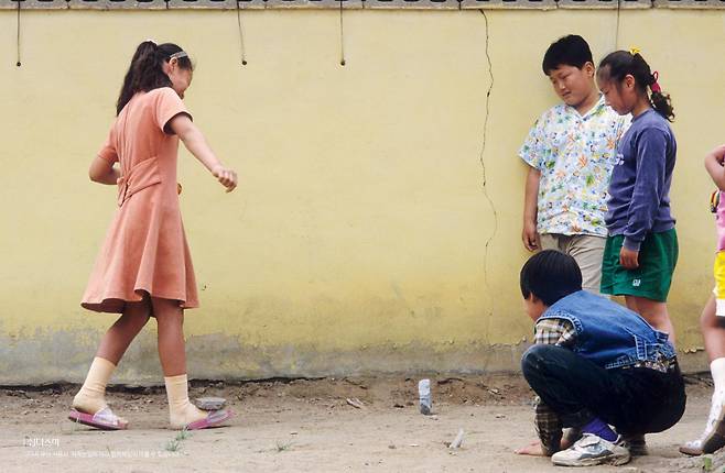 In this undated photo, children play biseok chigi (hitting a stone slab). Here shows the girl on the left carrying a rock on the top of her foot. [ENCYCLOPEDIA OF KOREAN FOLK CULTURE]