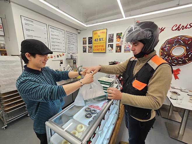 Samet Yesiltas receives a box of donuts to deliver from the owner of 42nd Street Donuts. (Choi Jae-hee/The Korea Herald)