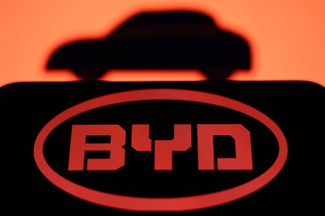 An illustrative image features a car positioned above a black screen displaying the BYD logo. (Getty Images)