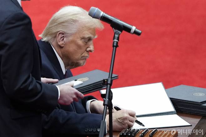[워싱턴=AP/뉴시스] 도널드 트럼프 미국 대통령이 20일(현지 시간) 워싱턴 캐피털 원 아레나에서 열린 실내 대통령 취임 퍼레이드 행사 중 행정명령에 서명하고 있다. 트럼프 대통령은 무대 한 편에 마련된 책상에서 행정명령에 줄줄이 서명했다. 2025.01.21. /사진=민경찬