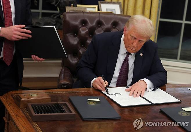콜라버튼 옆에 두고 서명 20일(현지시간) 행정명령에 서명하는 도널드 트럼프 미국 대통령. 책상 구석에 서명용 펜이 담긴 쟁반과 함께 '콜라 버튼'으로 추정되는 상자 모양의 물건이 놓여 있다. [로이터=연합뉴스]