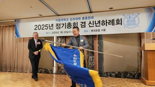 권영수 신임 서울대 상대 동창회장이 조문순 현 회장으로부터 상대기를 인도 받고 흔들고 있다. (출처=서울상대동창회보)