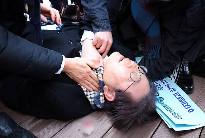 지난해 1월 2일 더불어민주당 이재명 대표가 부산 강서구 가덕신공항 부지를 둘러본 뒤 왼쪽 목 부위 피습을 당해 바닥에 누워 병원 호송을 기다리고 있다. 부산=연합뉴스