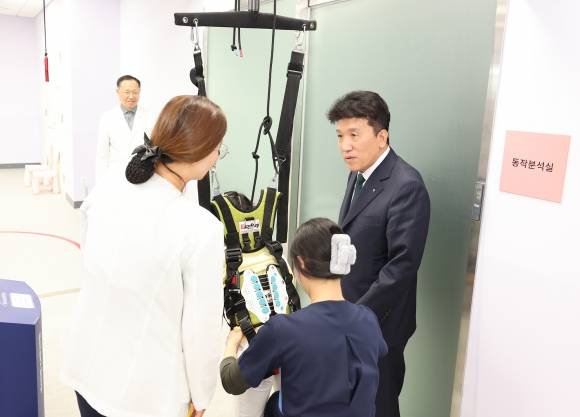 함영주 하나금융지주 회장(맨 오른쪽)이 17일 서울 마포구 푸르메재단 넥슨어린이재활병원에서 워킹레일 보행치료를 받고 있는 장애아동을 격려하고 있다. 하나금융지주 제공