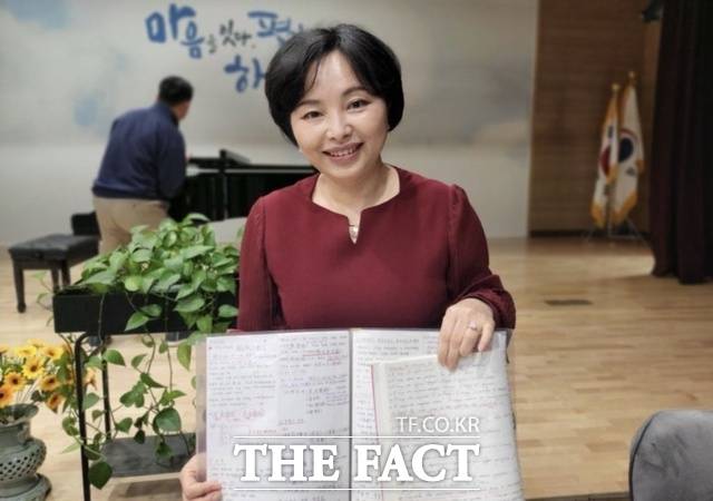 최 씨가 자원봉사과정으로 다문화 가정의 청소년들에게 한글을 가르치면서 적었던 한글연습 노트를 강의 중에 청중들에게 보여 주고 있다. / 최금희