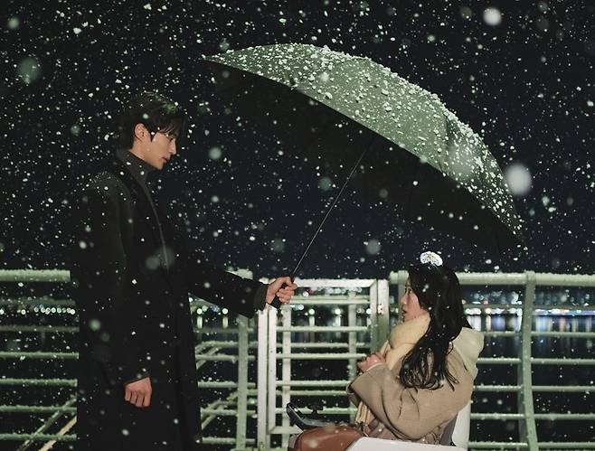 In a scene from the tvN romance series "Lovely Runner," Ryu Sun-Jae (left) holds an umbrella over Im Sol, who is in a wheelchair, on a snowy night. (tvN)