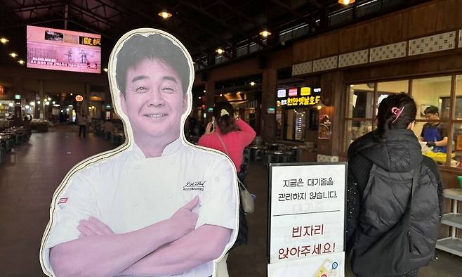 지난 10일 오후 충남 예산상설시장 광장 입구에 세워진 백종원 더본코리아 대표의 사진 입간판 옆으로 방문객들이 들어서고 있다. 송인걸 기자