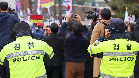 지난달 28일 서울 종로구 성균관대 앞에서 열린 윤석열 대통령 탄핵 반대 집회 측 스피커 앞에 선 경찰들이 귀를 막고 있다. 연합뉴스