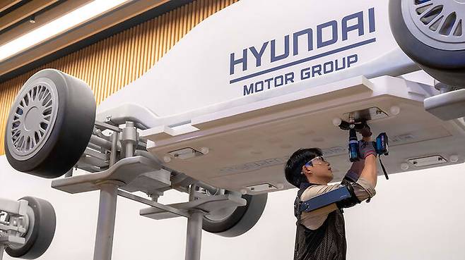 ▲ 상완 근력을 보조하는 현대자동차·기아의 착용 로봇 '엑스블 숄더'를 착용한 로보틱스랩 연구원이 팔을 올려 모형 차량 하부의 부품을 체결하고 있다.