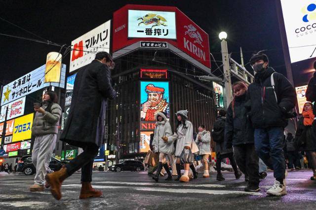 시민들이 지난달 17일 일본 홋카이도 삿포로의 명소인 스스키노 위스키 대형 광고판 밑을 지나가고 있다. 삿포로=AFP 연합뉴스