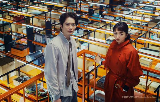 글로벌 쇼핑 사이트 '데일리 패스트(Daily Fast)' 관동지사의 팀 매니저 나시모토 코우(왼쪽, 오카다 마사키)와 센터장으로 부임한 후나도 엘레나(미쓰시마 히카리). 둘의 뒤로 물건들이 컨베이어 벨트에 실려 이동하고 있다. 사진 블루라벨픽쳐스