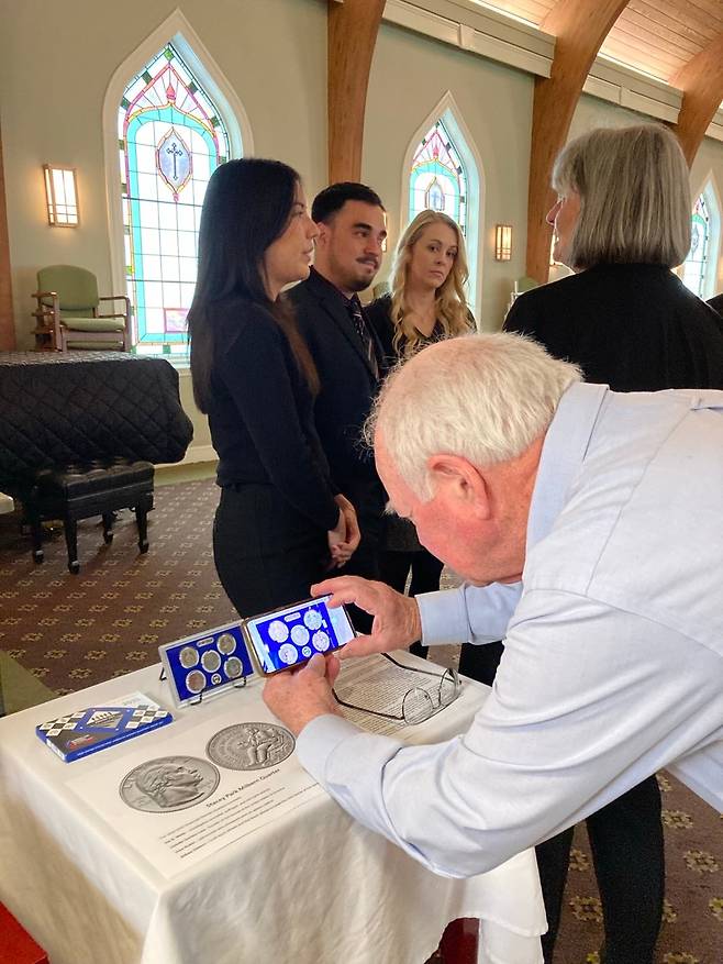 /스테이시 박 밀번 가족지난 15일 열린 뷸라 밀번의 영결식장을 찾은 추모객들이 스테이시 박 밀번의 얼굴을 새긴 동전 기념세트를 촬영하고 있다.