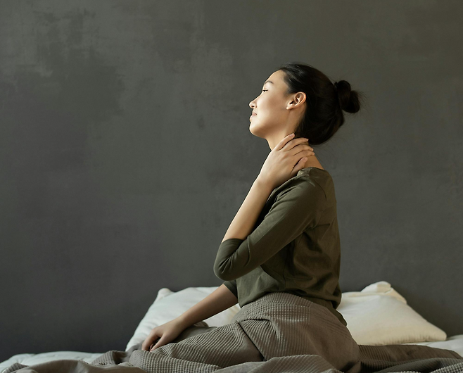 왼손으로 목을 잡고 왼쪽을 바라보고 앉아있는 여성