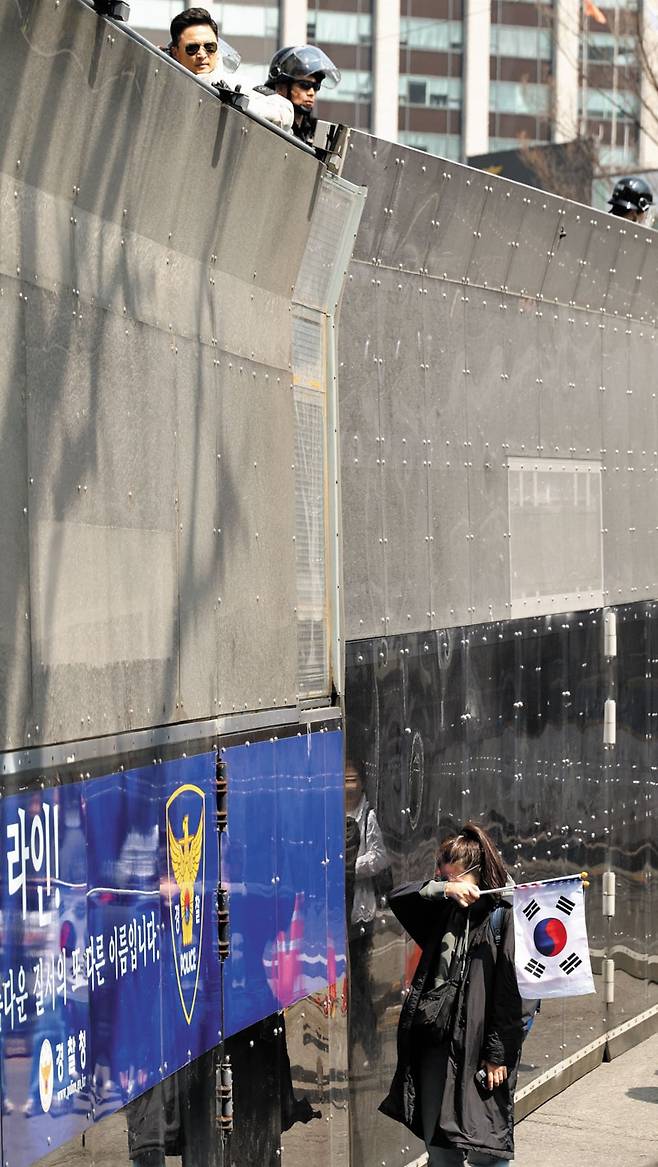 방어벽 앞 눈물 흘리는 尹 지지자 - 헌법재판소가 4일 윤석열 대통령 파면 결정을 내리자 태극기를 든 지지자가 경찰이 세운 방어벽 앞에서 눈물을 흘리고 있다. 경찰이 높이 4m 방어벽 위에서 경비를 서고 있다. 경찰은 이날 물리적 충돌에 대비해 헌법재판소 주변을 플라스틱 방어벽과 경찰 버스 등으로 막았다. /연합뉴스