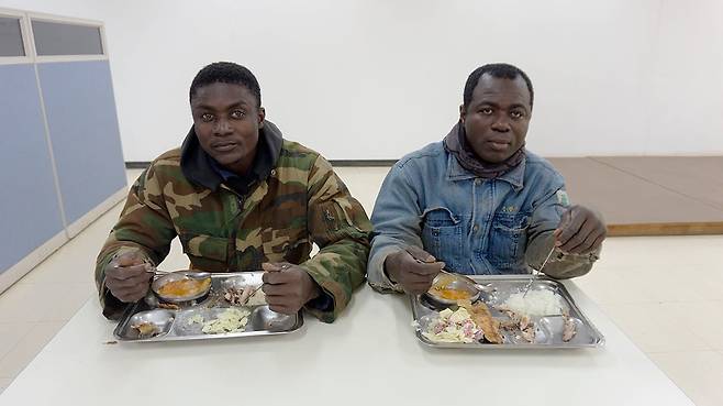 경기도 화성의 철 구조물 공장 구내식당에서 나란히 앉아 밥을 먹는 두명의 가나 출신 외국인 노동자. 3백명이 넘게 앉을 수 있는 큰 식당에서 이들은 늘 구석에 앉아 식사를 했다. 2017년/ 사진가 심학철