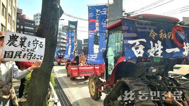 3월30일 일본 도쿄 도심에서 트랙터들이 정부에 농정 대개혁을 촉구하며 줄을 지어 행진하고 있다. 한 시민이 트랙터 행진을 응원하며 ‘농업을 지키는 것은 국민을 지키는 것’이라는 팻말을 들고 있다.