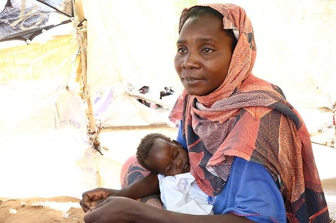 남수단 난민촌서 임시 거주하는 수단 난민 (렌크[남수단]=연합뉴스) 성도현 기자 = 수단 난민 수사 아스마일 씨(오른쪽)가 지난달 26일(현지시간) 남수단 국경 지역 난민촌 TC2에서 그의 막내아들(왼쪽)을 안고 지원 내용을 설명하고 있다. 2025.4.11 raphael@yna.co.kr