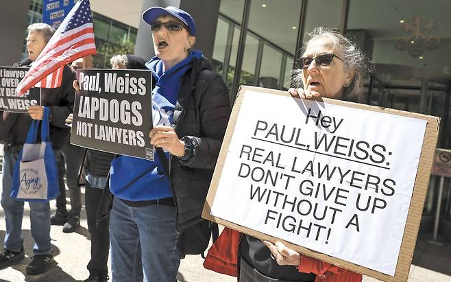 "진짜 변호사는 싸워보지도 않고 포기 안 한다" - 지난 2일 미국 뉴욕의 로펌 '폴 와이스(Paul Weiss)' 앞에서 반(反)트럼프 시위대가 "진짜 변호사들은 싸우지도 않고 포기하지 않는다" "변호사가 아닌 애완견"같은 팻말을 들고 시위를 하고 있다. 트럼프가 과거 자신에게 호의적이지 않았던 이 로펌 소속 변호사들의 연방 정부 보안 인가를 박탈하자, 로펌은 트럼프 행정부에 무료 법률 서비스를 제공하기로 하면서 굴복했다. /EPA 연합뉴스