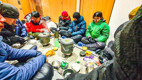 저녁을 먹기 위해 다 함께 화장실 바닥에 둘러앉았다. 한쪽에서는 마실 물을 만들기 위해 눈을 끓이고 있고, 다른 한쪽에서는 밥을 짓고 있다.