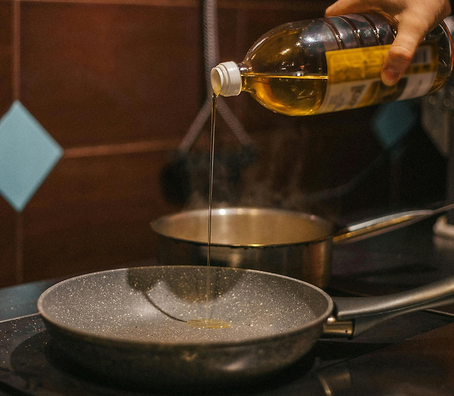 후라이팬에 투명한 병에 들어있는 노란 기름을 따르는 손