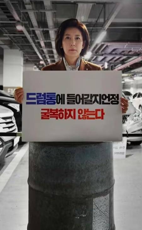 Na poses standing in a steel barrel holding a sign that says, “I’d rather get into a drum barrel than surrender.” (Na’s Facebook page)