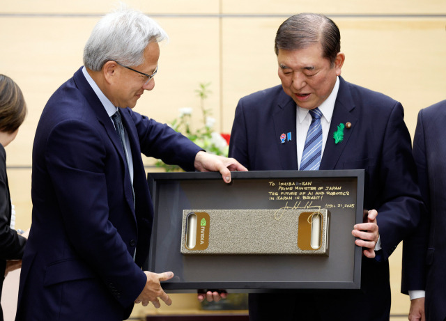 이시바 시게루(오른쪽) 일본 총리가 21일 도쿄 총리실에서 젠슨 황 엔비디아 최고경영자(CEO)로부터 일본의 인공지능(AI)과 로보틱스의 미래를 응원한다는 메모와 사인이 새겨진 기념품을 선물받고 있다. AP연합뉴스