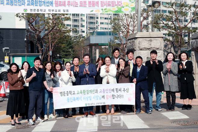 지난 21일 용인 영문중학교 관계자와 학부모들이 통학차량 승하차베이 조성사업을 지원한 이상일 용인특례시장의 방문을 환영하는 현수막을 들고 기념사진을 찍고 있다.(사진=독자제공)