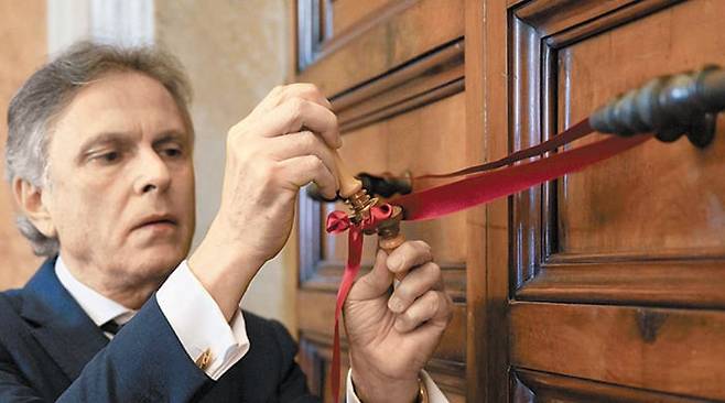 교황청 관계자가 21일 바티칸 내 사도궁 3층에 있는 프란치스코 교황 집무실 문 손잡이를 붉은색 리본으로 묶어 봉쇄하고 있다. 전임 교황들은 사도궁을 관저로도 사용했지만 프란치스코 교황은 ‘산타 마르타의 집’에 거주하며 이곳으로 출퇴근했다. 산타 마르타의 집에 있는 교황 숙소도 함께 봉쇄됐다. /AFP 연합뉴스