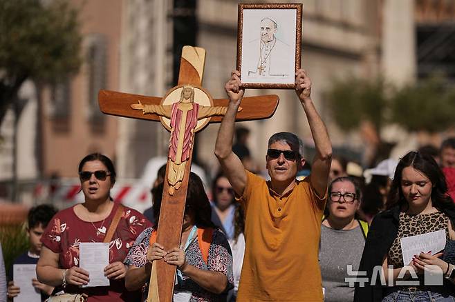 [바티칸=AP/뉴시스] 22일(현지 시간) 바티칸 성 베드로 광장에서 십자가와 프란치스코 교황 사진을 든 사람들이 행진하고 있다. 바티칸은 프란치스코 교황의 장례식을 오는 26일 오전 10시(한국 시간 오후 5시)에 거행하기로 하고, 교황의 시신이 안치된 관이 성 베드로 대성당으로 옮겨지는 23일부터 일반 신자들의 공개 조문을 받기로 했다. 2025.04.23.