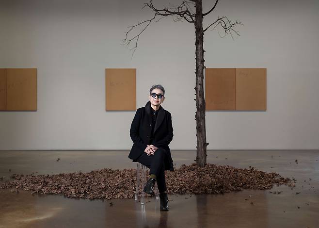 최재은 작가가 숲의 생명력을 펼친 K2 전시장 1층에 앉았다. 뒤에 걸린 회화 연작은 교토의 숲에서 모은 낙엽과 꽃잎으로 물감을 만들고 캔버스에 칠한 뒤 바람소리, 새소리, 빗소리를 그대로 음차해 흑연으로 적었다. 사진 안천호. /국제갤러리