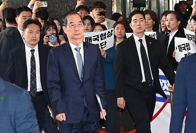 한덕수 대통령 권한대행 국무총리가 24일 오전 국회에서 2025년도 1회 추가경정예산안에 관한 시정연설을 위해 본회의장으로 걸어가고 있다. 구 야권 의원들이 한 대행에게 한미 통상 협상을 중단하라고 요구하는 팻말을 들고 시위하고 있다. /뉴스1