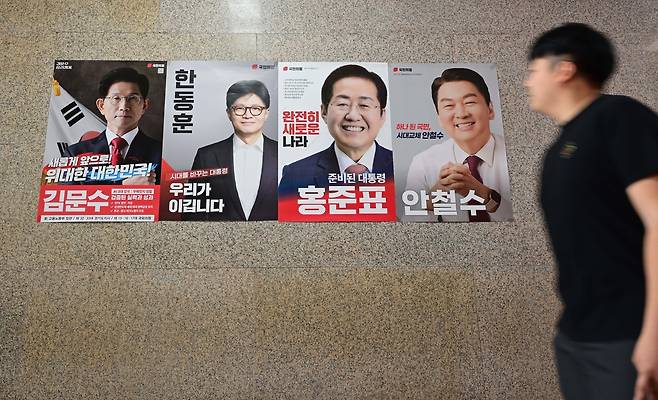 A man walks past posters on a wall at the National Assembly in Seoul on Wednesday featuring the four remaining candidates who have passed the first round of the conservative People Power Party's primary for its nomination in the June 3 presidential election. From left are former Labor Minister Kim Moon-soo, former party leader Han Dong-hoon, former Daegu Mayor Hong Joon-pyo and lawmaker Rep. Ahn Cheol-soo.  (Lee Sang-sub/The Korea Herald)