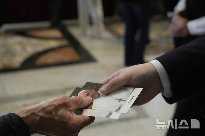 [바티칸시국=AP/뉴시스] 23일(현지 시간) 성베드로 대성당에서 열린 프란치스코 교황의 일반 신자 조문에 참여한 조문객이 교황의 사진을 건네 받고 있다. 교황의 시신은 사흘간 대성당에 안치돼 일반 신자들의 조문을 받는다. 2025.04.24.