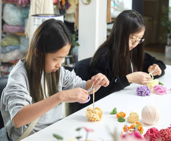 소중 학생기자단이 바늘로 뜨개질해서 편편한 꽃을 모아 꽃송이 모양처럼 만들고 있다.