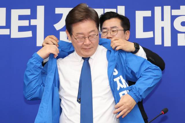 더불어민주당 박찬대 당대표 직무대행 겸 원내대표가 28일 서울 여의도 국회에서 열린 최고위원회의에서 이재명 대선 후보에게 선거운동용 파란색 점퍼를 입혀주고 있다. 연합뉴스