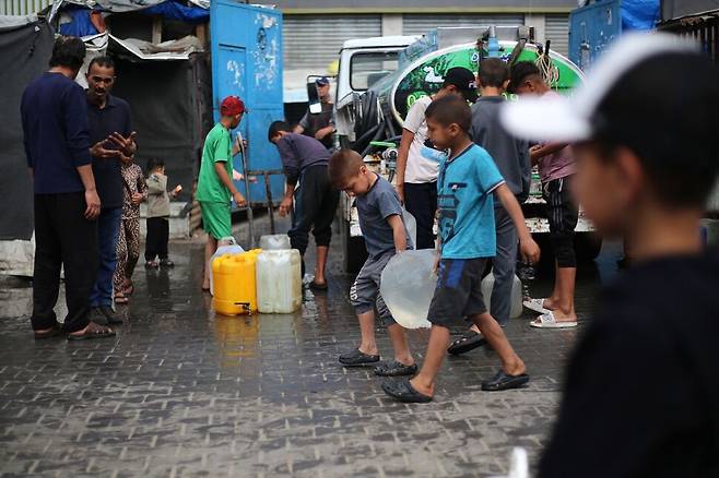 28일(현지시각) 팔레스타인 소년들이 가자지구 중부 브레이즈 난민캠프에서 물을 담아 걸어가고 있다. 브레이즈/AFP 연합뉴