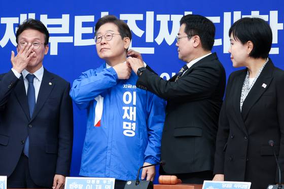 박찬대 더불어민주당 대표 직무대행 겸 원내대표가 28일 서울 여의도 국회에서 열린 최고위원회의에서 이재명 대선 후보에게 선거복을 입혀준 뒤 옷깃을 정리하고 있다. 뉴스1