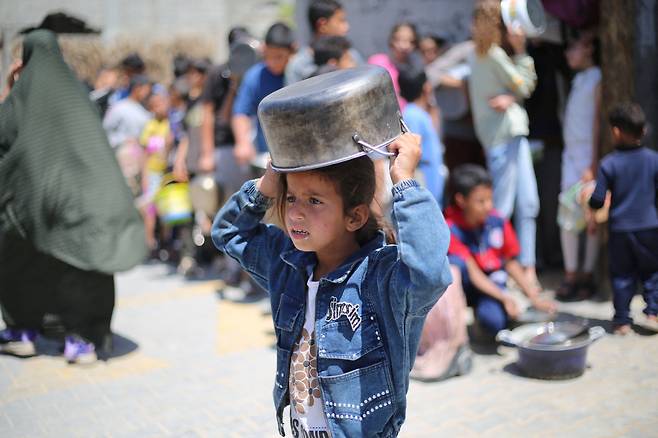 29일 한 팔레스타인 어린이가 가자지구 중부의 부레이 난민 캠프 급식소에서 음식을 타기위해 냄비를 머리에 쓰고 기다리고 있다./AFP 연합뉴스