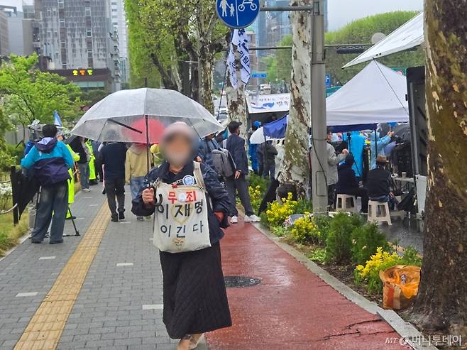 1일 대법원 건너편 '무죄 이재명 이긴다'는 문구를 몸에 두른 여성이 '유죄 취지 파기환송' 선고 후 무표정으로 우산을 쓴 채 걸어가고 있다./사진=이혜수 기자